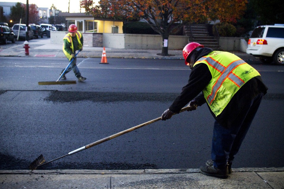 Two workers in safety gear using hand tools to smooth pavement.